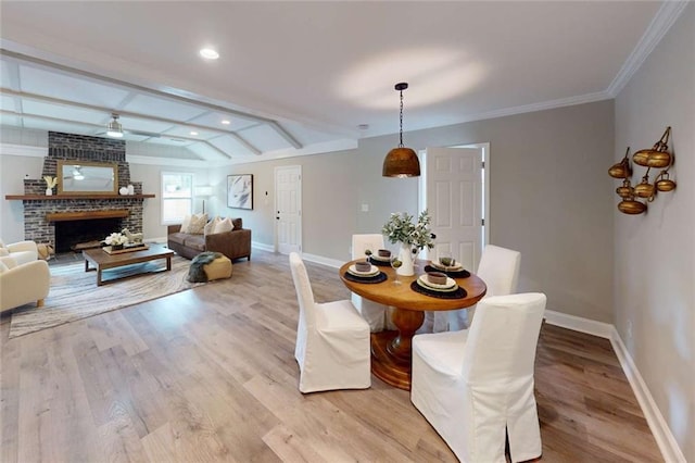 dining area featuring crown molding, a brick fireplace, light wood-style floors, and baseboards