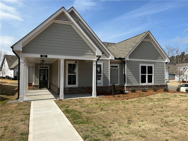 view of front of property featuring brick siding, a porch, a front yard, and a shingled roof