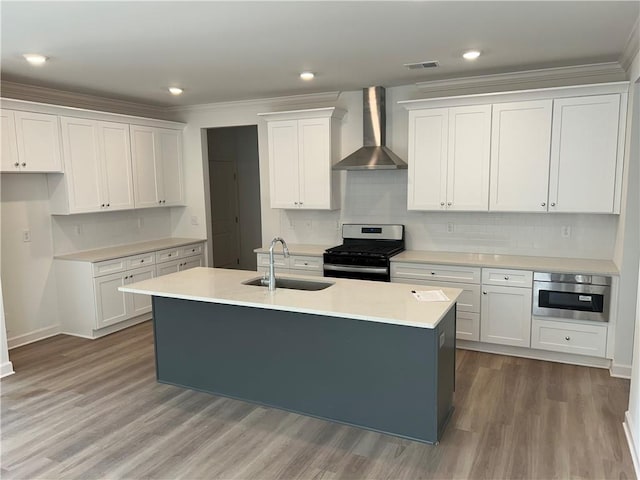 kitchen featuring a center island with sink, a sink, white cabinetry, gas stove, and wall chimney range hood