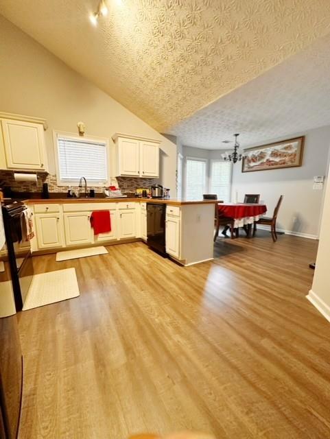 kitchen featuring light hardwood / wood-style floors, black dishwasher, vaulted ceiling, kitchen peninsula, and a textured ceiling