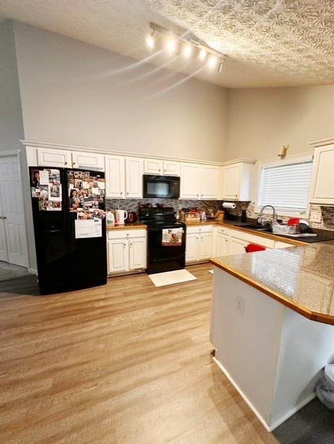 kitchen with light wood-type flooring, black appliances, white cabinetry, and a towering ceiling