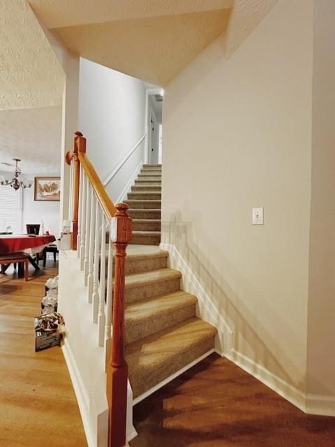 stairs featuring wood-type flooring and a notable chandelier