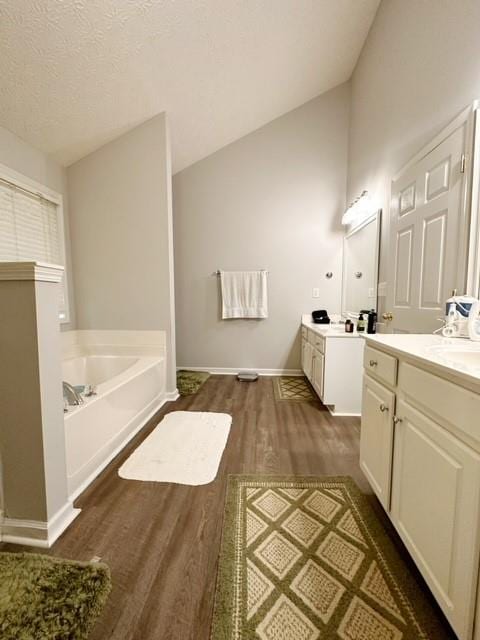 bathroom featuring vanity, lofted ceiling, a bath, wood-type flooring, and a textured ceiling