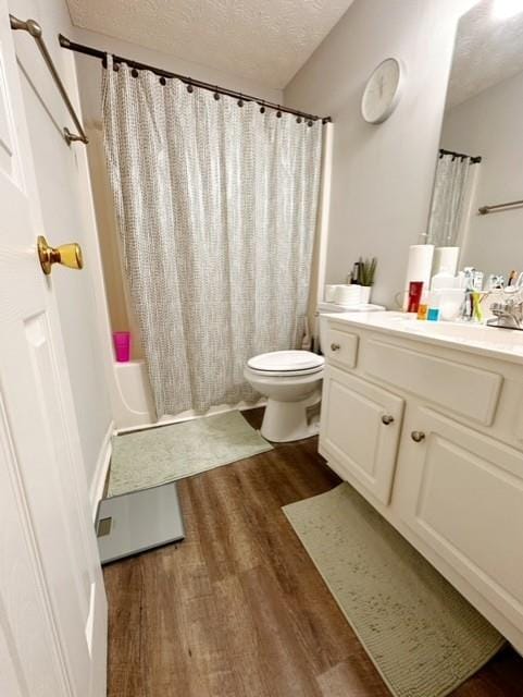 full bathroom with shower / tub combo with curtain, hardwood / wood-style floors, vanity, toilet, and a textured ceiling