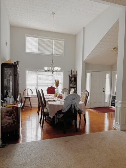 dining space with wood-type flooring, a high ceiling, a notable chandelier, and a textured ceiling