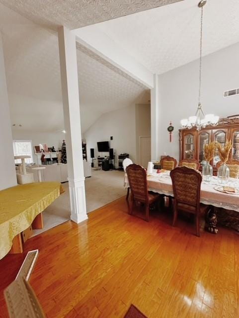 dining room featuring hardwood / wood-style floors, vaulted ceiling, an inviting chandelier, and a textured ceiling