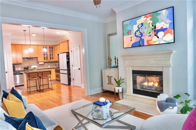 living room featuring light wood-type flooring, ornamental molding, a glass covered fireplace, and baseboards