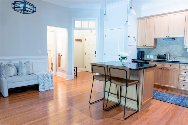 kitchen with a breakfast bar area, dark countertops, light wood finished floors, a kitchen island, and crown molding
