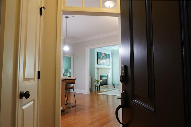 foyer entrance with ornamental molding, a glass covered fireplace, wood finished floors, and baseboards