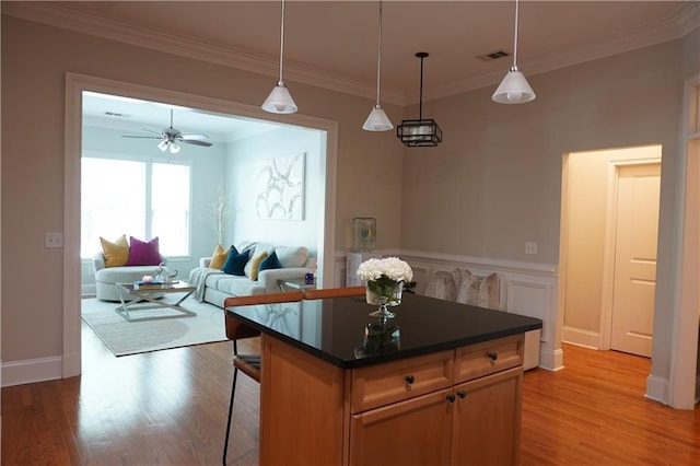 kitchen featuring light wood-type flooring, dark countertops, hanging light fixtures, and ornamental molding