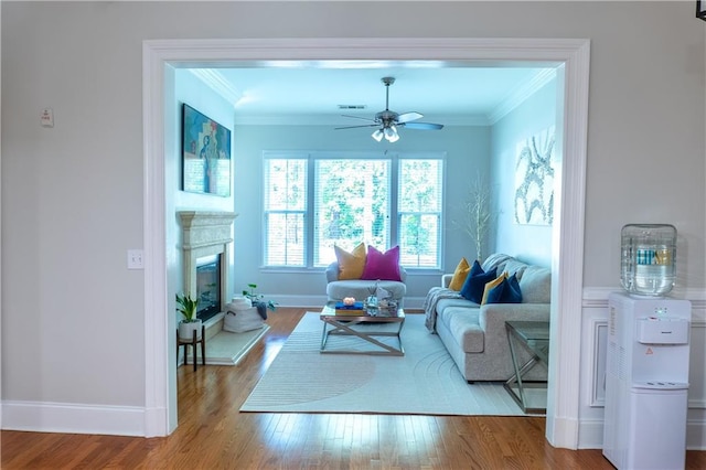 living room with ornamental molding, ceiling fan, baseboards, wood finished floors, and a glass covered fireplace