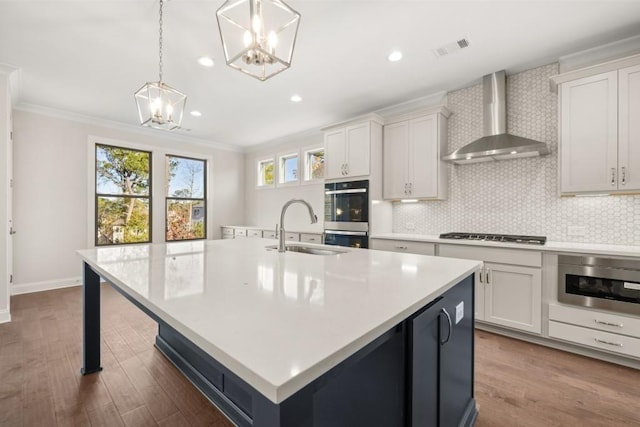 kitchen with visible vents, wall chimney range hood, a sink, appliances with stainless steel finishes, and a notable chandelier