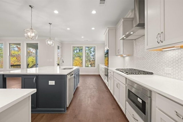 kitchen featuring wall chimney range hood, crown molding, a sink, a kitchen island with sink, and visible vents