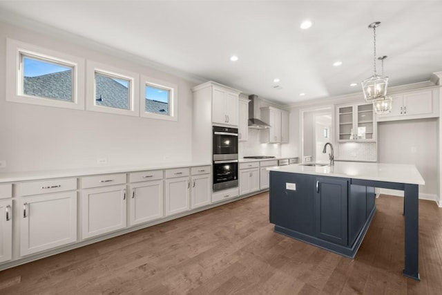 kitchen with decorative backsplash, a sink, white cabinets, double oven, and wall chimney exhaust hood
