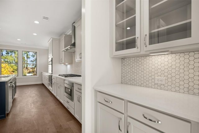 kitchen featuring light countertops, glass insert cabinets, and wall chimney exhaust hood