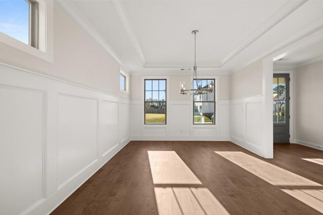 unfurnished dining area with an inviting chandelier, dark wood-type flooring, a decorative wall, and a tray ceiling