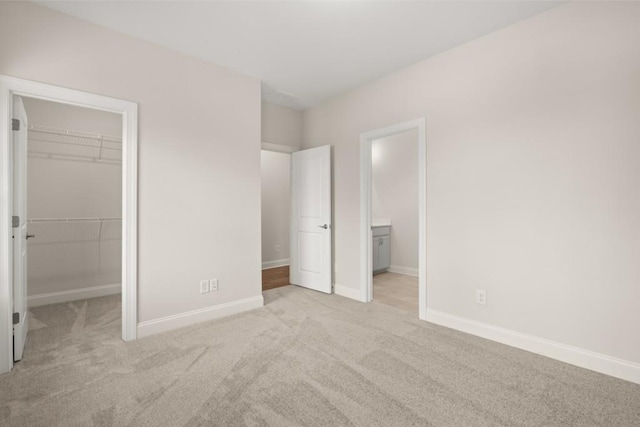 unfurnished bedroom featuring baseboards, a closet, connected bathroom, a spacious closet, and light carpet