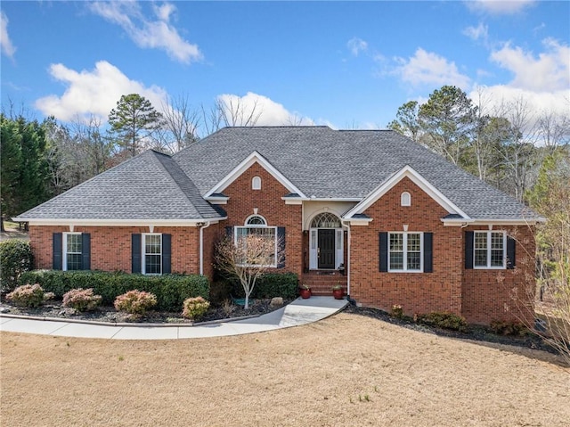 view of front of home with brick siding, a front lawn, and a shingled roof