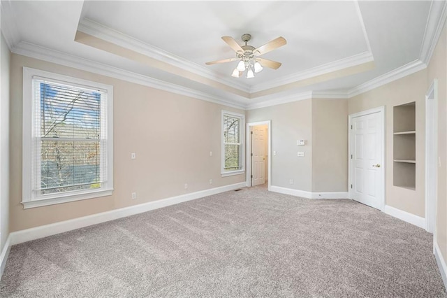 unfurnished bedroom with a raised ceiling, multiple windows, light colored carpet, and baseboards