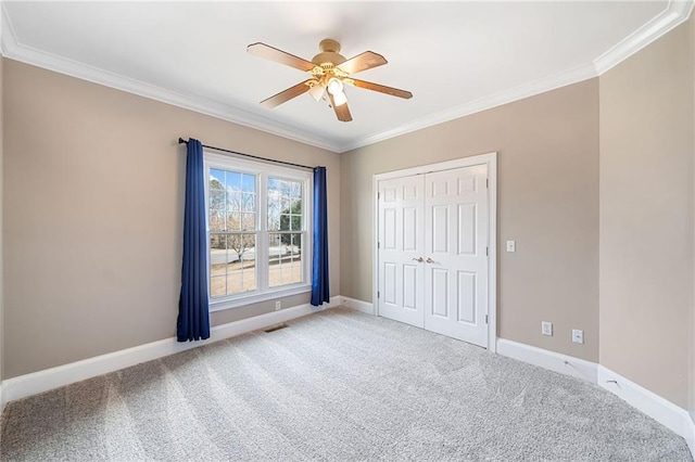 empty room featuring ceiling fan, light colored carpet, baseboards, and ornamental molding