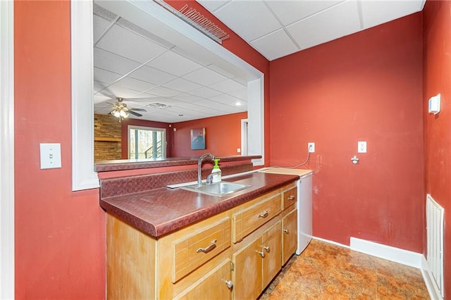 kitchen featuring a ceiling fan, a sink, dark countertops, a paneled ceiling, and baseboards