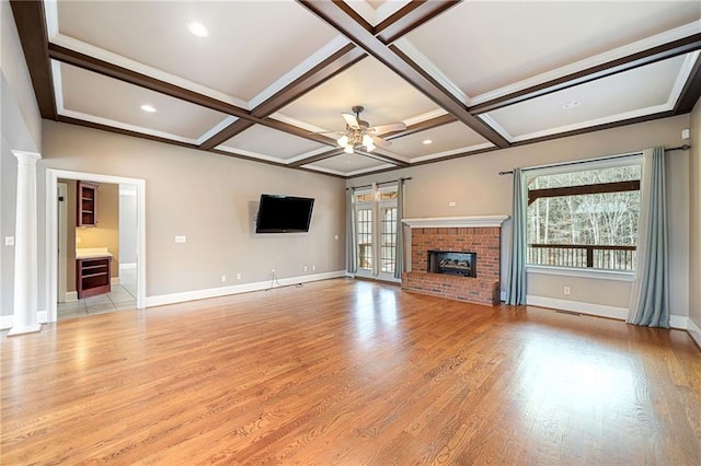 unfurnished living room featuring light wood-type flooring, coffered ceiling, a fireplace, ceiling fan, and ornate columns