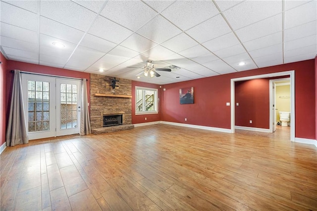 unfurnished living room with light wood-type flooring, a ceiling fan, a drop ceiling, a fireplace, and baseboards