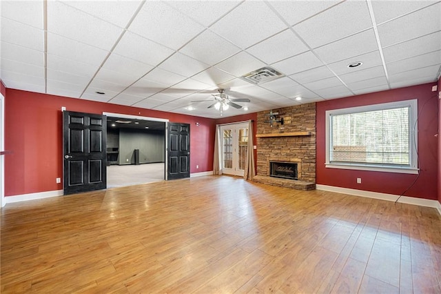 unfurnished living room with visible vents, a drop ceiling, wood finished floors, a stone fireplace, and baseboards