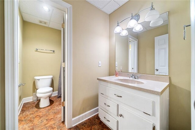 half bathroom featuring a drop ceiling, toilet, vanity, and baseboards