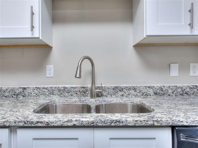 kitchen with white cabinetry, black dishwasher, light stone counters, and sink