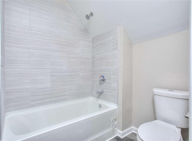 bathroom featuring toilet, vaulted ceiling, and tiled shower / bath