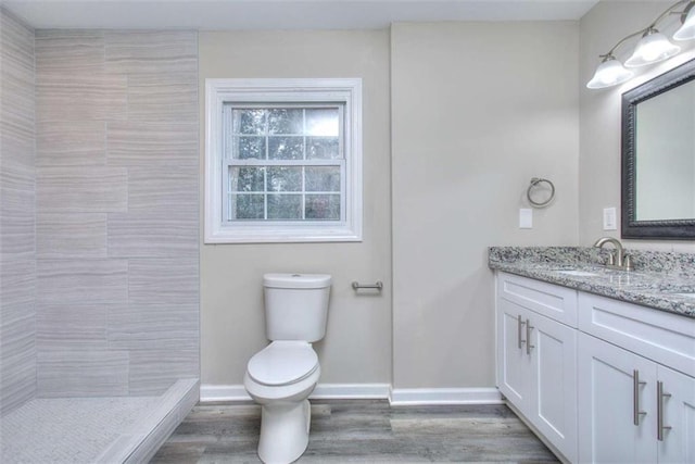 bathroom with wood-type flooring, toilet, vanity, and a tile shower