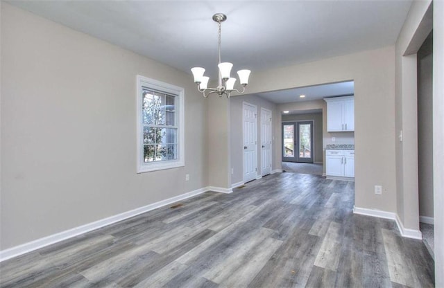 unfurnished dining area featuring dark wood-type flooring, an inviting chandelier, and french doors