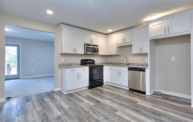 kitchen with light wood-type flooring, appliances with stainless steel finishes, white cabinets, and light stone counters