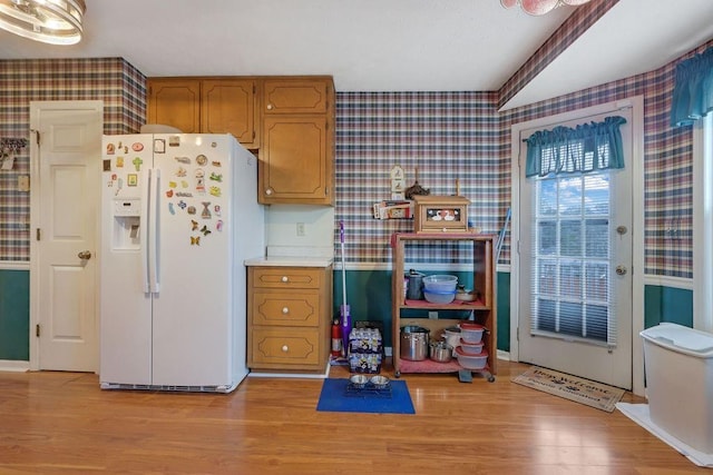 kitchen with white fridge with ice dispenser, light countertops, light wood-style flooring, and wallpapered walls