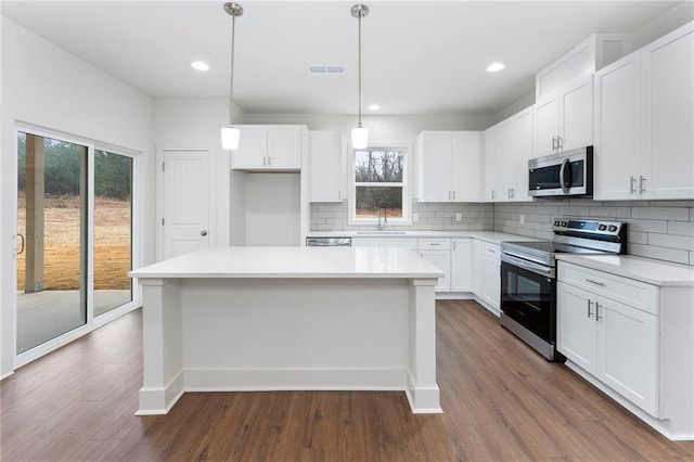 kitchen with a kitchen island, white cabinets, pendant lighting, stainless steel appliances, and backsplash