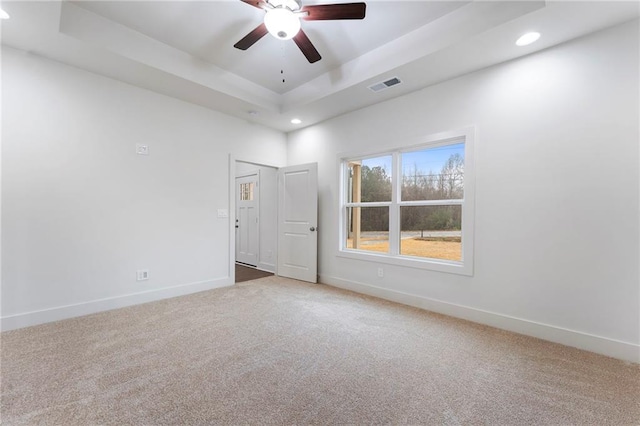 carpeted spare room featuring ceiling fan and a raised ceiling