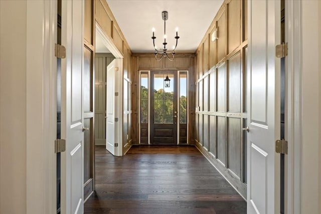 interior space with wood walls, dark wood finished floors, and an inviting chandelier