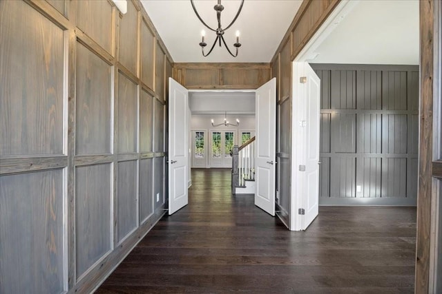 corridor featuring a decorative wall, dark wood-style flooring, stairway, and an inviting chandelier