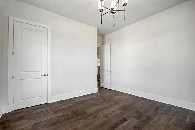 unfurnished room with dark wood-type flooring, a chandelier, and baseboards