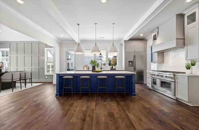 kitchen with a breakfast bar area, appliances with stainless steel finishes, dark wood-type flooring, a center island, and premium range hood