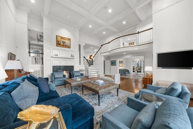 living room featuring wood finished floors, coffered ceiling, a high ceiling, stairs, and a large fireplace