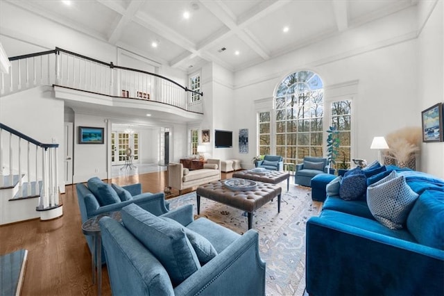 living room featuring wood finished floors, coffered ceiling, stairs, a towering ceiling, and beamed ceiling