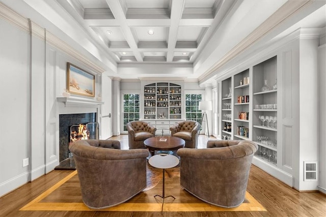 sitting room featuring beam ceiling, coffered ceiling, wood finished floors, and a fireplace