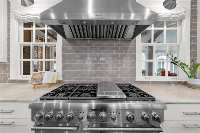 kitchen with decorative backsplash, range with two ovens, exhaust hood, and white cabinets