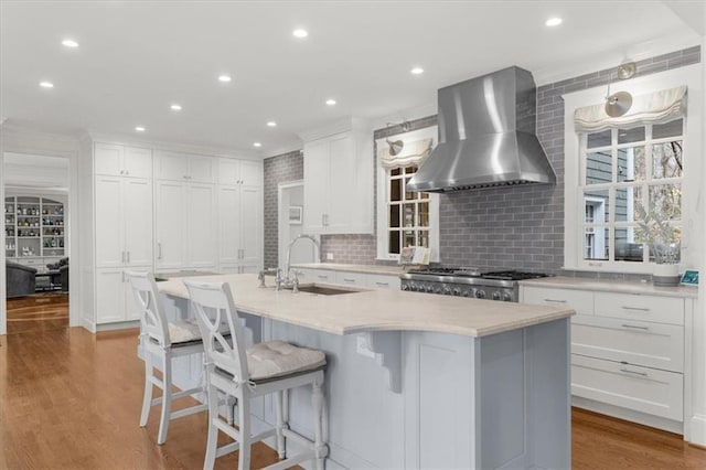 kitchen featuring a sink, wall chimney range hood, light wood-style flooring, white cabinets, and range