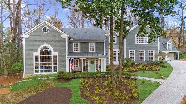 shingle-style home with a porch, a chimney, decorative driveway, and a garage