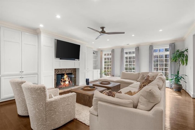living room featuring dark wood-type flooring, crown molding, ceiling fan, recessed lighting, and a fireplace