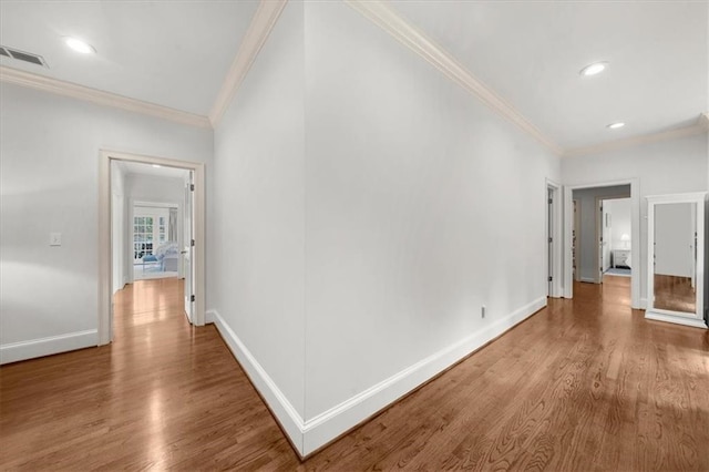 hallway featuring visible vents, ornamental molding, baseboards, and wood finished floors