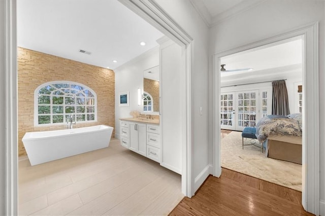 full bath with vanity, wood finished floors, a soaking tub, ornamental molding, and french doors